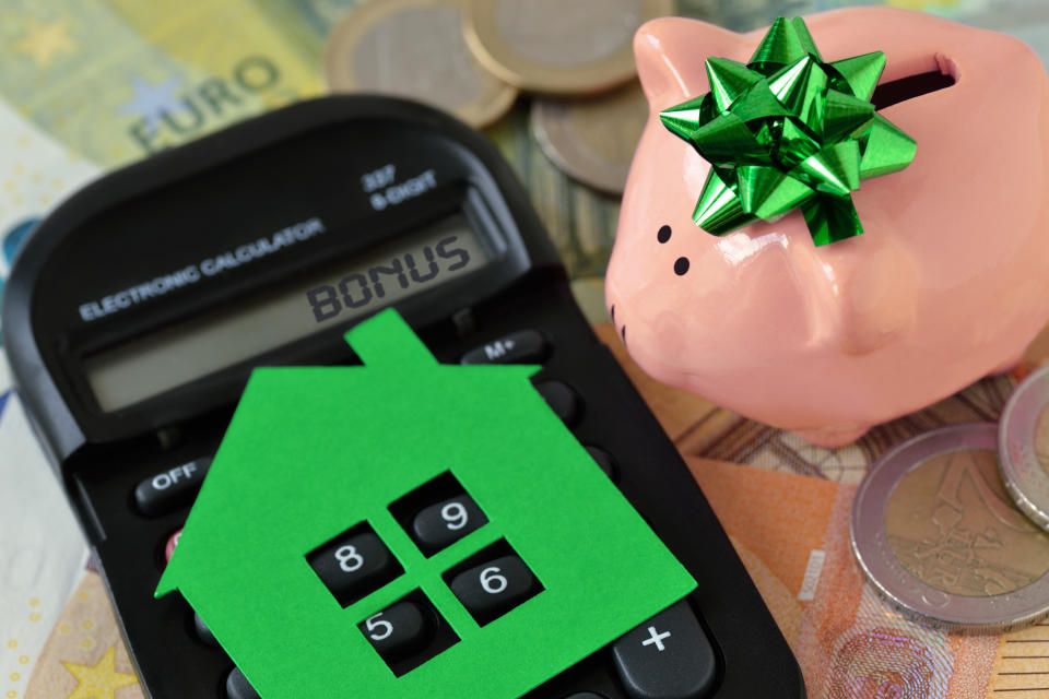 Piggy bank with calculator and paper house on euro money background - Concept of saving money to buy a home and money bonus