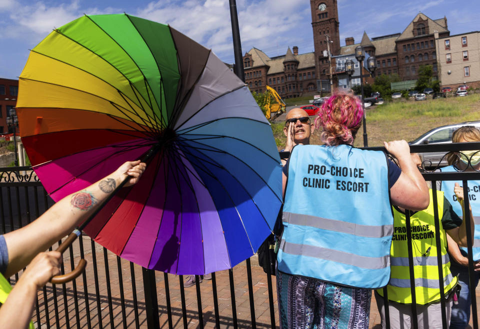 Clinic escorts deploy umbrellas and their bodies to block the view of anti-abortion protester Tom Schaer, center, wearing dark glasses, as he shouts at a woman entering the clinic, Thursday, July 7, 2022 at WE Health Clinic in Duluth, Minn. (AP Photo/Derek Montgomery)