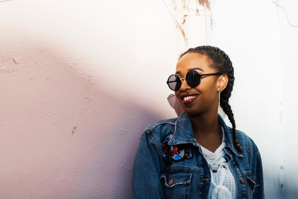 <h1 class="title">Smiling young woman wearing sunglasses and denim jacket standing by white wall</h1><cite class="credit">Alexandra C. Ribeiro</cite>