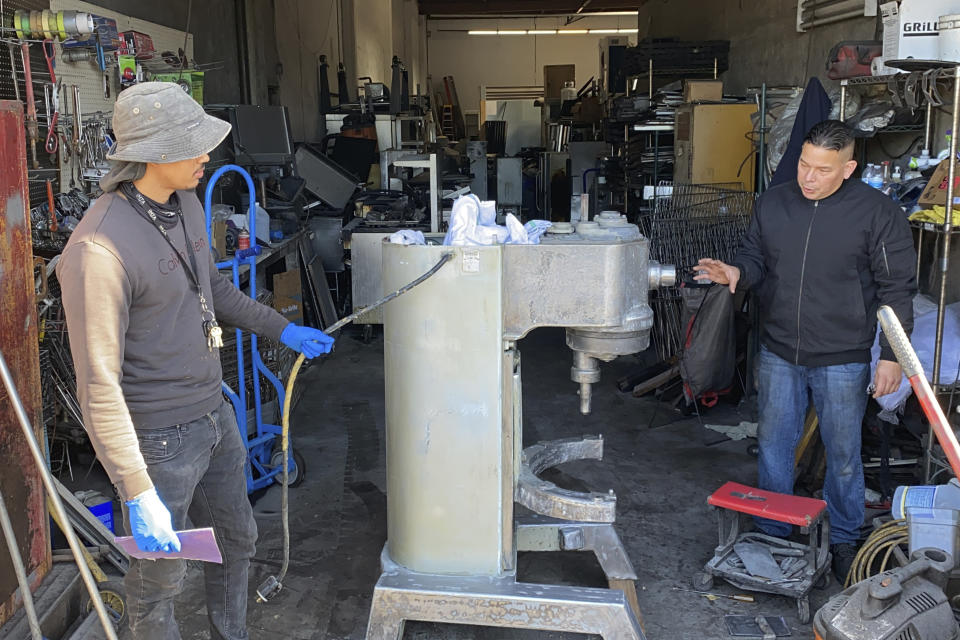 Jose Bonilla Jr., right, talks to an employee about cleaning a used industrial mixer for sale at the warehouse of his family's business, American Restaurant Supply in San Leandro, Calif., on Jan. 14, 2021. The pandemic has forced thousands of restaurants to permanently shut their doors as dining restrictions keep customers away. But the unprecedented closures have created a business boom for commercial auctioneers that buy and sell used restaurant equipment. (AP Photo/Terry Chea)