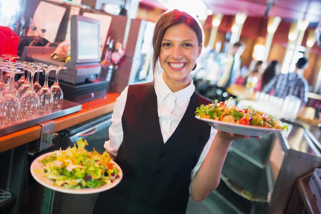 barmaid holding plates of salads in a bar