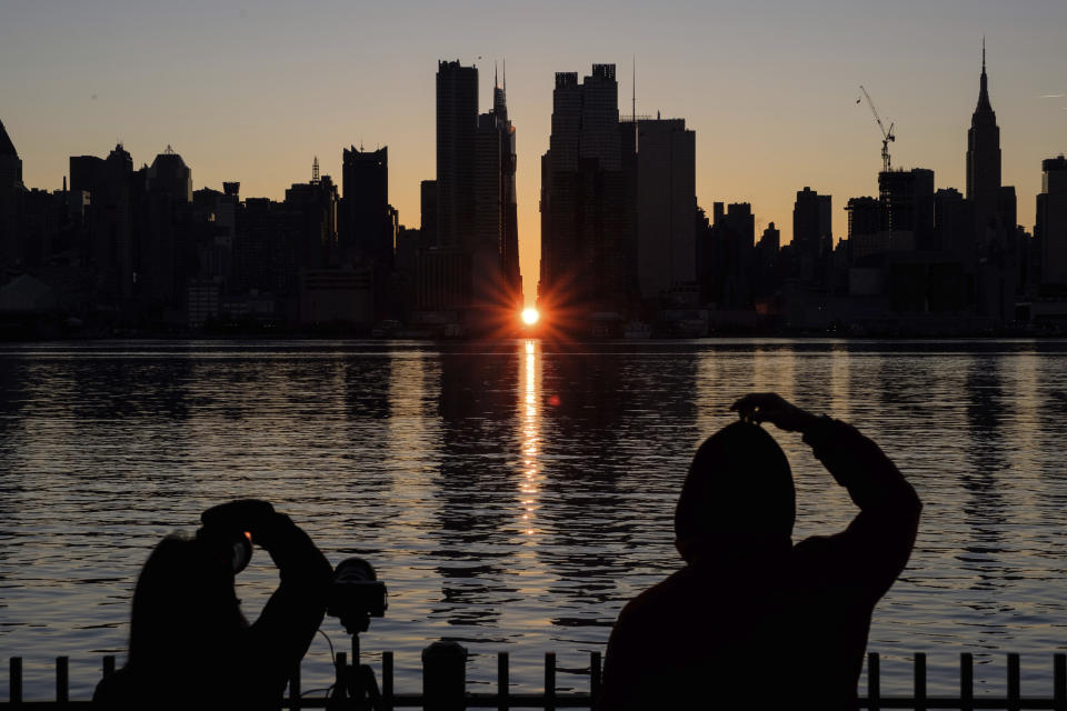 People view a Manhattanhenge sunrise along 42nd street in New York's Manhattan borough on Sunday, Nov. 29, 2020, as viewed from Weehawken, N.J. There's still time to catch Manhattanhenge, when the setting sun aligns with the Manhattan street grid and bathes the urban canyons in a rosy glow. The last two Manhattanhenge sunsets of 2022 are Monday and Tuesday, July 11-12. (AP Photo/Yuki Iwamura, File)