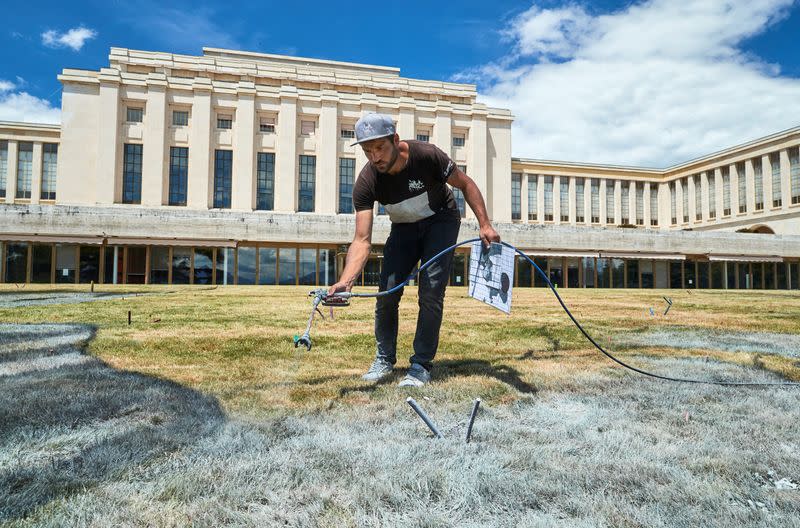 El artista francés Saype rocía una mezcla ecológica de tiza y carbón para crear una obra de arte que representa a dos niños arrodillados en un círculo mientras dibujan un árbol para conmemorar el 75 aniversario de la fundación de Naciones Unidas en el césped de su sede europea en Ginebra, Suiza