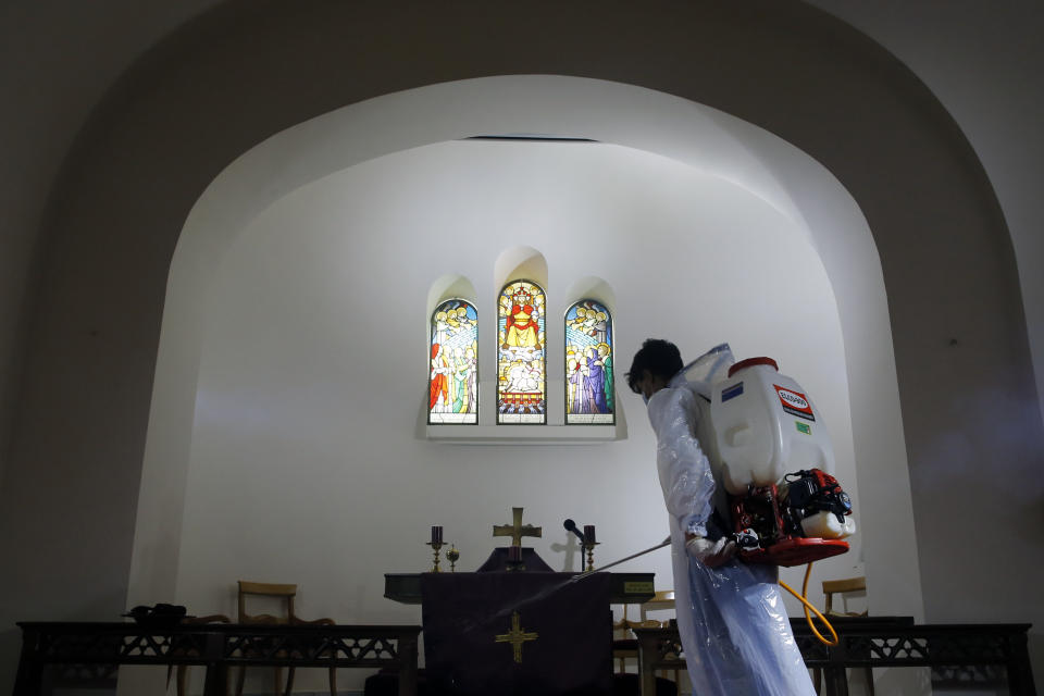 A municipal worker wearing protective gear sprays spray disinfectant as a precaution against the coronavirus, at a church in Beirut, Lebanon, Sunday, March 22, 2020. Lebanon has been taking strict measures to limit the spread of the coronavirus closing restaurants and nightclubs as well as schools and universities. (AP Photo/Bilal Hussein)