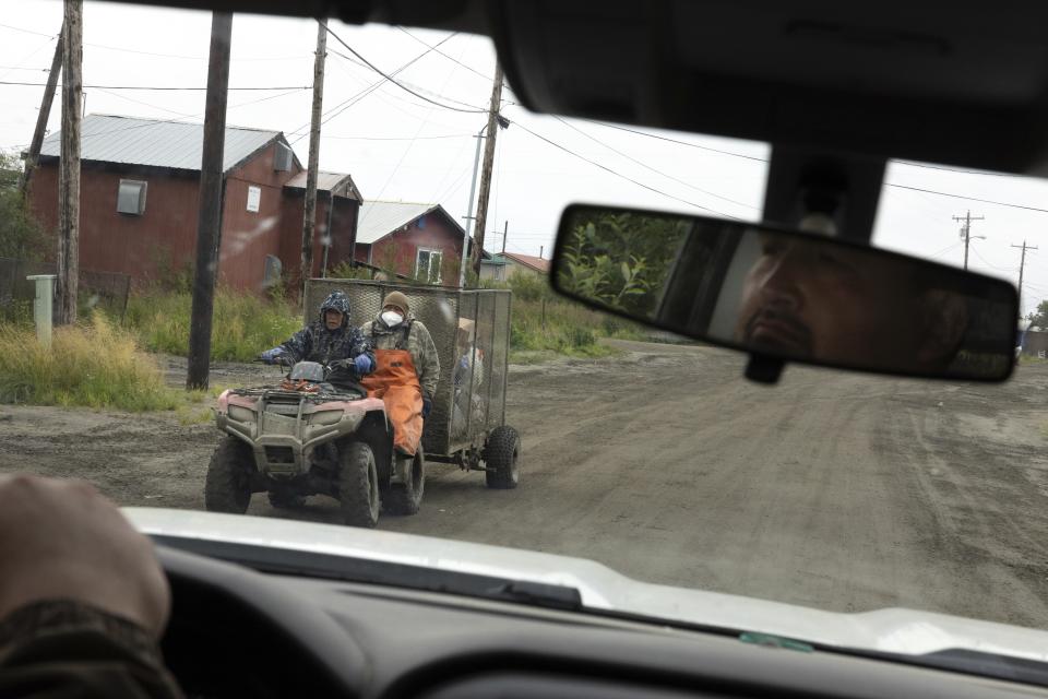 Thomas Noatak, alongside Joseph Moses, carry garbage across Phillips Street during morning pickup, Thursday, Aug. 17, 2023, in Akiachak, Alaska. Each morning, Noatak and Moses ride through the village to collect near-capacity honey buckets and trash bins for disposal. (AP Photo/Tom Brenner)