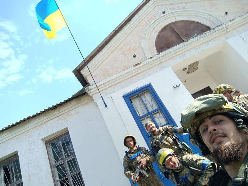 Service members pose for a picture with a Ukrainian national flag in the village of Vasylenkove, recently liberated by Ukrainian Armed Forces in Kharkiv region