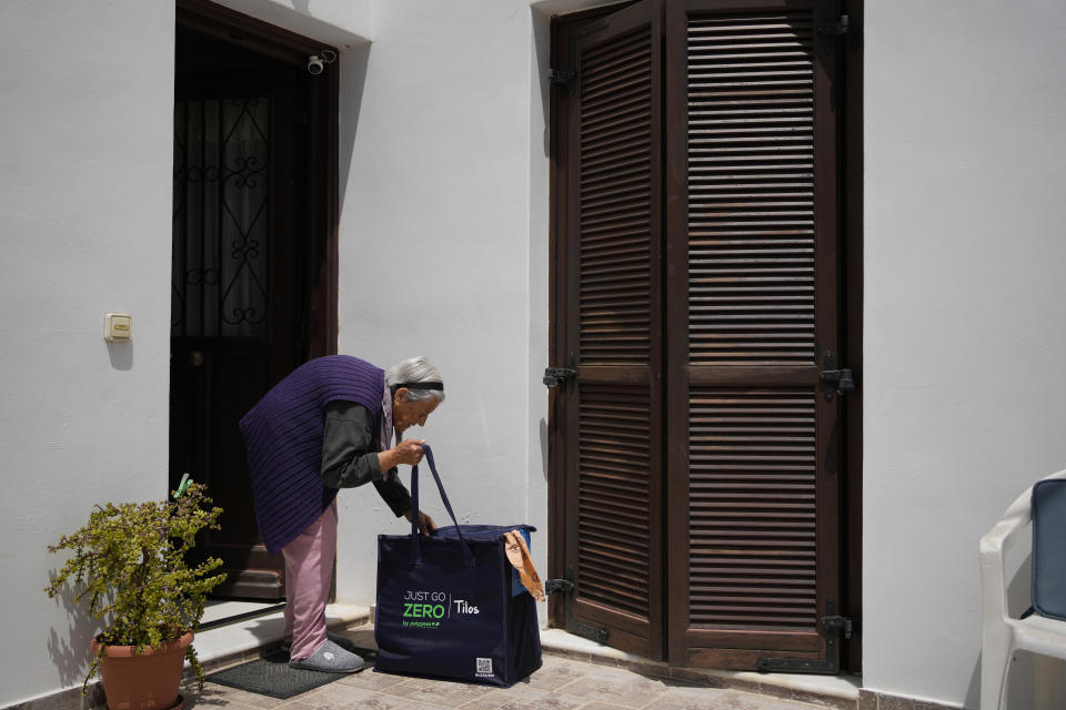 An elderly woman takes a recycling bag after workers collected trash from her house on the Aegean Sea island of Tilos, southeastern Greece, Monday, May 9, 2022. When deciding where to test green tech, Greek policymakers picked the remotest point on the map, tiny Tilos. Providing electricity and basic services, and even access by ferry is all a challenge for this island of just 500 year-round inhabitants. It's latest mission: Dealing with plastic. (AP Photo/Thanassis Stavrakis)