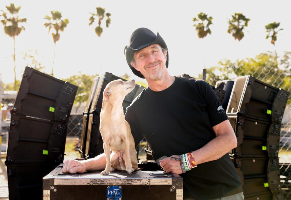 Man in black cowboy hat posing with small dog back stage at Coachella