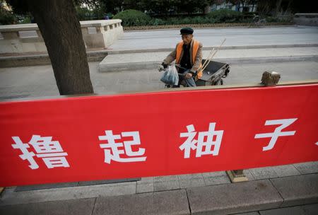 A cleaner is pictured behind a banner reading "Roll up sleeves to work hard" at Chang'an Avenue in central Beijing, as the capital prepares for the 19th National Congress of the Communist Party of China, October 13, 2017. REUTERS/Jason Lee