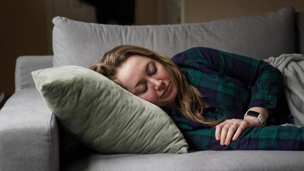  A woman lies on a sofa, eyes closed, under a blanket. 