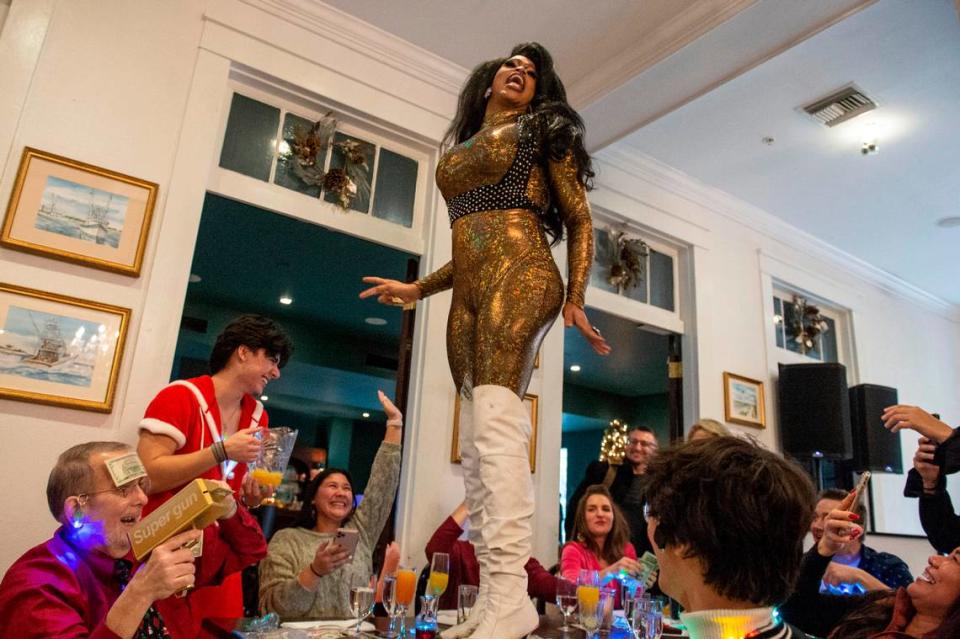 Lexis Redd D’ville stands on top a table where brunch guests dine on several courses of food and mimosas during drag brunch at White Pillars in Gulfport on Sunday, Dec. 19, 2021.