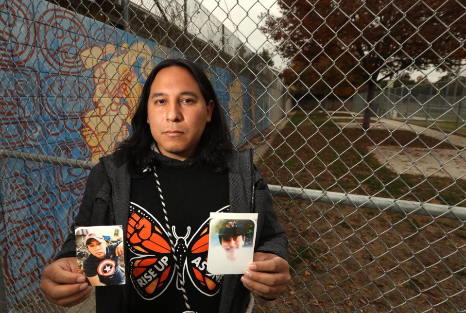 A man in front of a fence holds photos of two men.