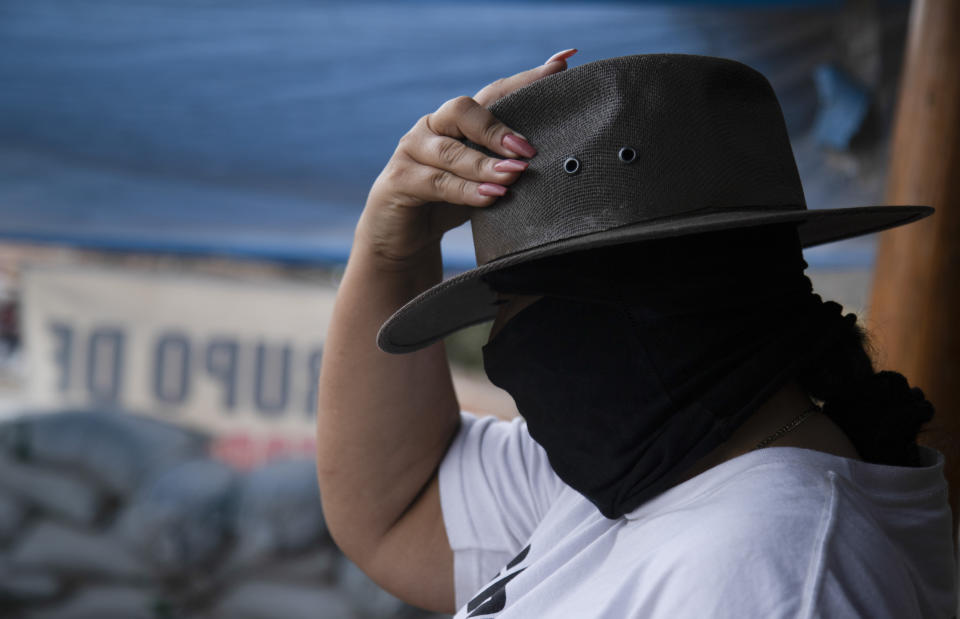 A masked woman who said she was displaced from her community by criminal groups adjusts her hat as she helps patrol a checkpoint run by a group of armed women who call themselves a self-defense group, at the entrance to El Terrero in Michoacan state, Mexico, Wednesday, Jan. 13, 2021. The rural area is traversed by dirt roads, through which they fear Jalisco gunmen could penetrate at a time when the homicide rate in Michoacán has spiked to levels not seen since 2013. (AP Photo/Armando Solis)