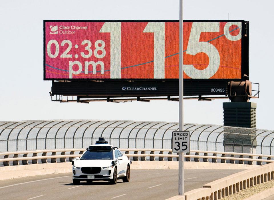 A Waymo self-driving car drives on Seventh Street as the temperature of 115 degrees is displayed on a digital billboard in downtown Phoenix on July 17, 2023. On July 27, Phoenix marked day 15 of 2023 with temperatures above 115 degrees.