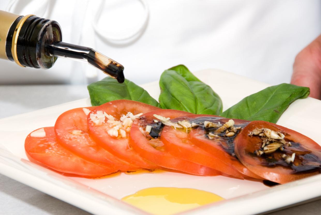 Chef decorating a plate with tomatos, basil, garlic, olive oil and balsamic vinegar