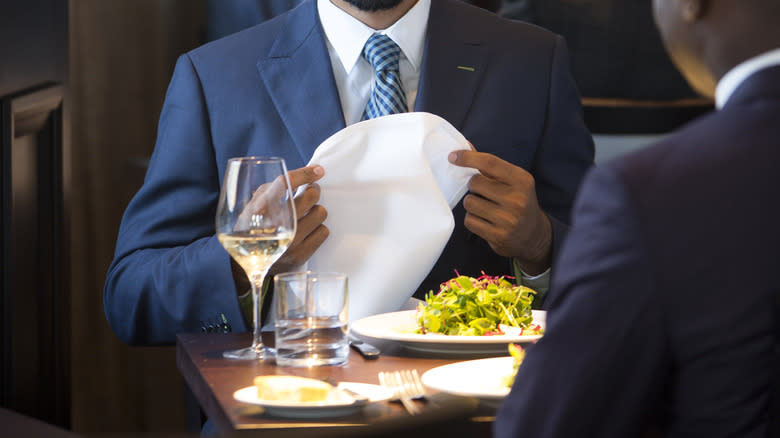 Man placing napkin in lap 