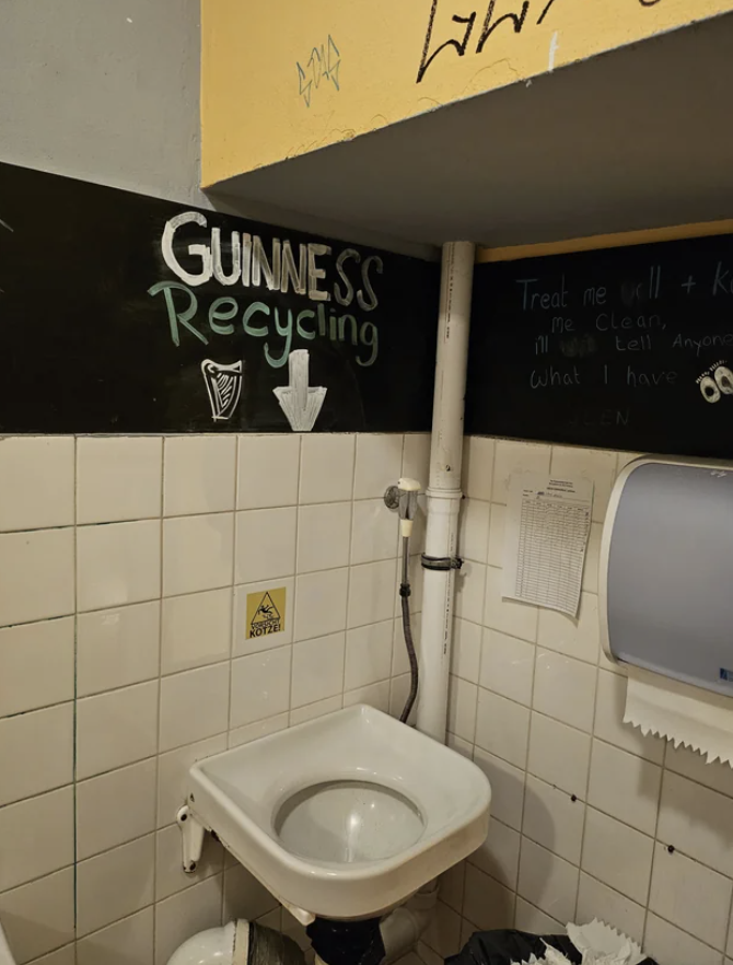 A restroom with a humorous sign "GUINNESS RECYCLING" pointing to a throwup sink