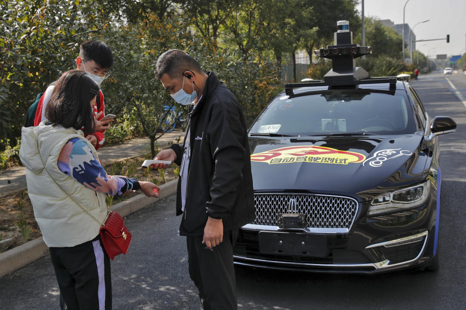 A couple wearing face masks to help curb the spread of the coronavirus gets temperature check before they try out the self-driving ride-hailing services by tech giant Baidu on the outskirts of Beijing on Oct. 15, 2020. Chinese leaders are shifting focus from the coronavirus back to long-term goals of making China a technology leader at this year's highest-profile political event, the meeting of its ceremonial legislature, amid tension with Washington and Europe over trade, Hong Kong and human rights. (AP Photo/Andy Wong)