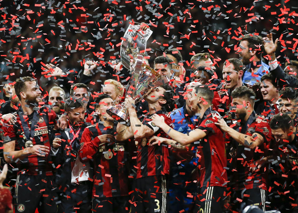 Atlanta United team captain Michael Parkhurst (3) kisses the trophy as teammates celebrate during the trophy presentation after the MLS Cup championship soccer game against the Portland Timbers, Saturday, Dec. 8, 2018, in Atlanta. Atlanta United won 2-0. (AP Photo/Todd Kirkland)