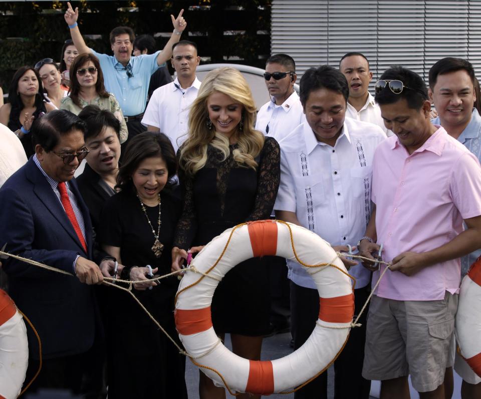 Paris Hilton, center, cuts the ribbon in a ceremony to unveil the Paris Beach Club, which she designed in collaboration with Philippine developer Century Properties Thursday, March 13, 2014 at suburban Paranaque city, southeast of Manila, Philippines. Paris Hilton unveiled her first real estate project Thursday in metropolitan Manila and said she wants to follow in the footsteps of her great-grandfather and grandfather, who led a luxury hotel empire. (AP Photo/Bullit Marquez)