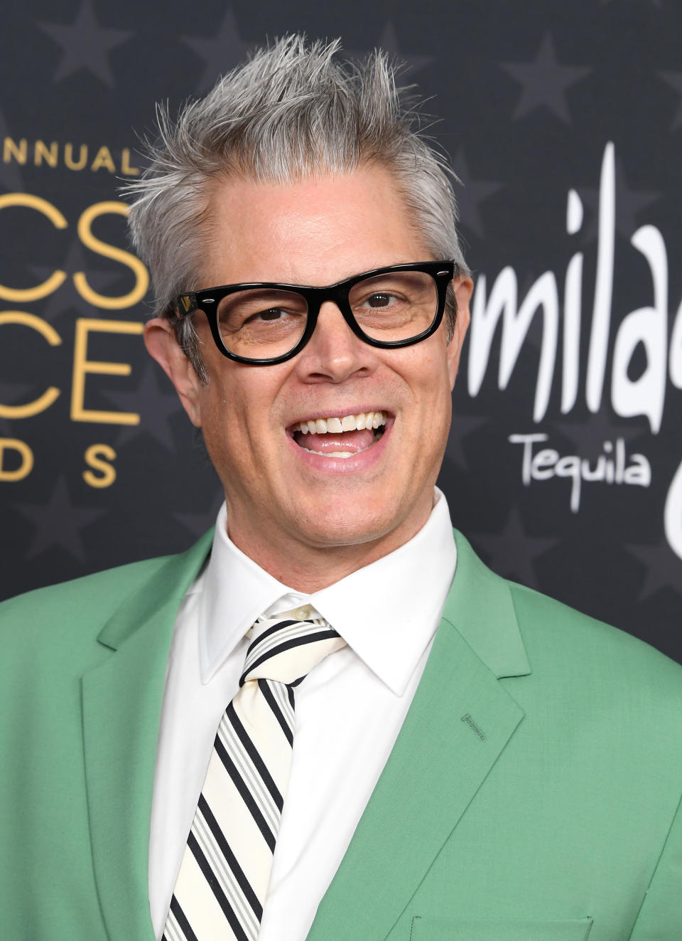 Close-up of Johnny/Philip smiling at a media event in a suit and striped tie