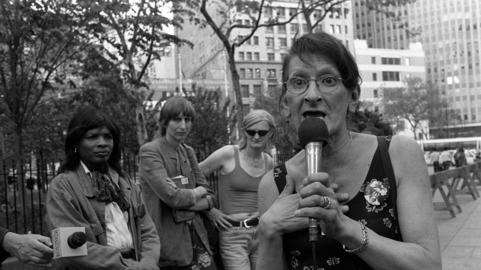 sylvia rivera speaking into a microphone at a rally as other attendees look on in the background