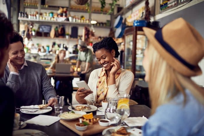 Group of friends enjoying food at a restaurant and using a mobile phone.