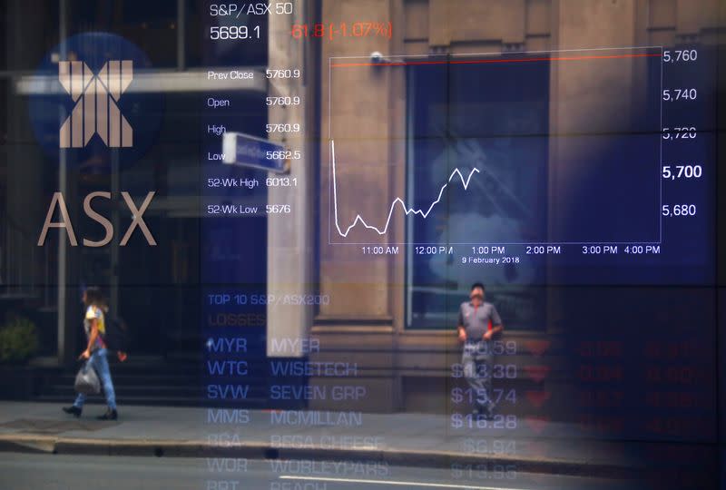 FILE PHOTO - Pedestrians are reflected in a window in front of a board displaying stock prices at the Australian Securities Exchange in Sydney