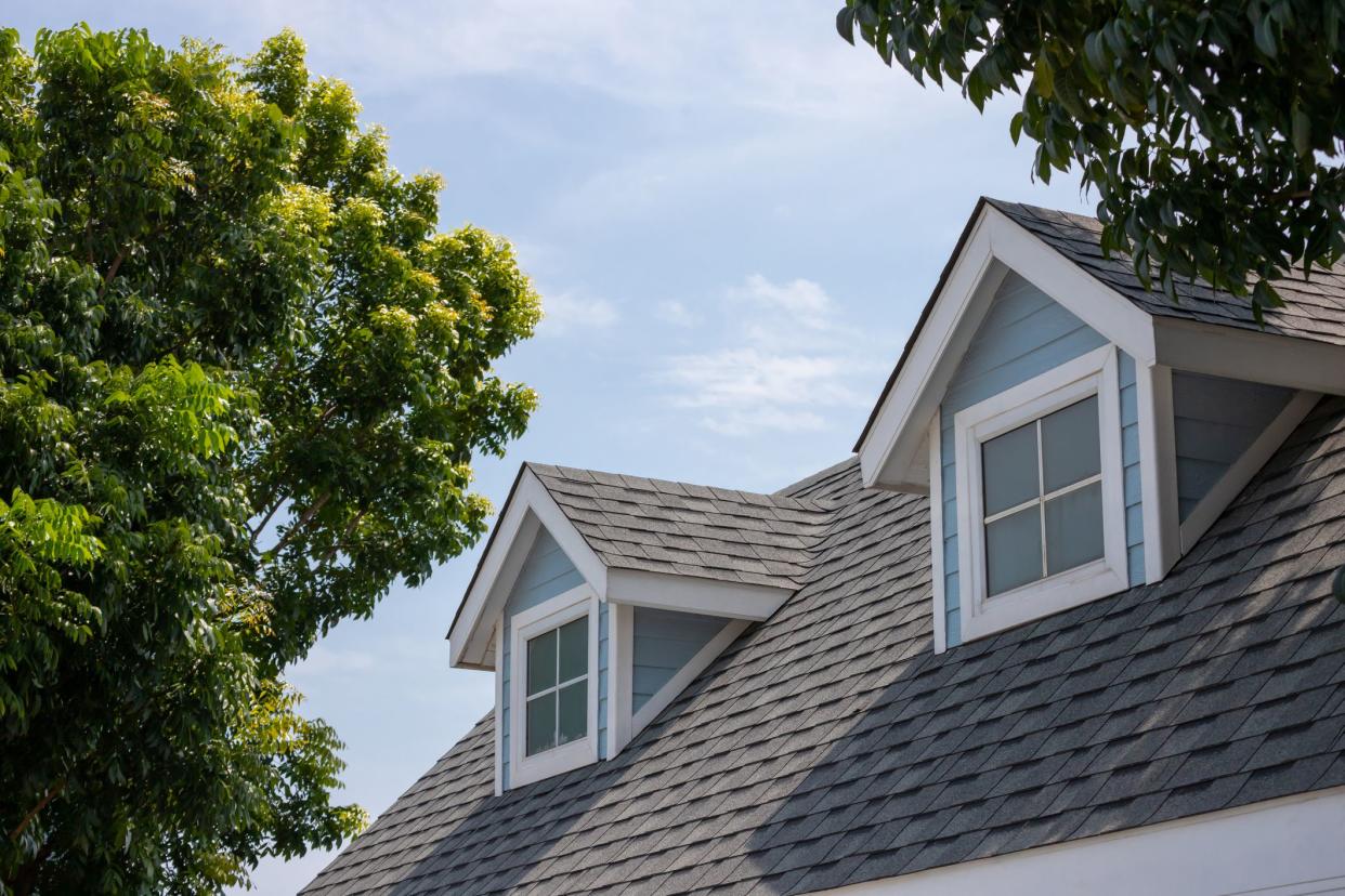 Roof shingles with garret house on top of the house among a lot of trees. dark asphalt tiles on the roof background.