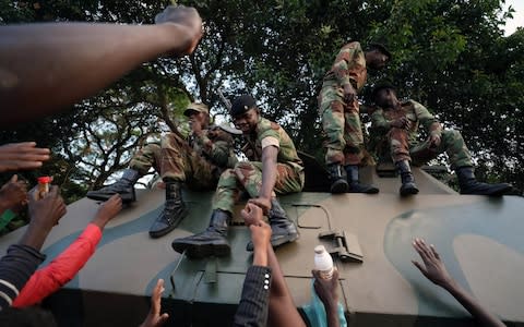 Demonstrators celebrating Mugabe's resignation reach to congratulate soldiers for their role - Credit:  MIKE HUTCHINGS/ REUTERS