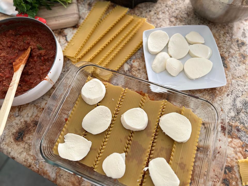 fresh mozzarella on lasagna noodles in a pan next to a pot of sauce and a plate of more cheese