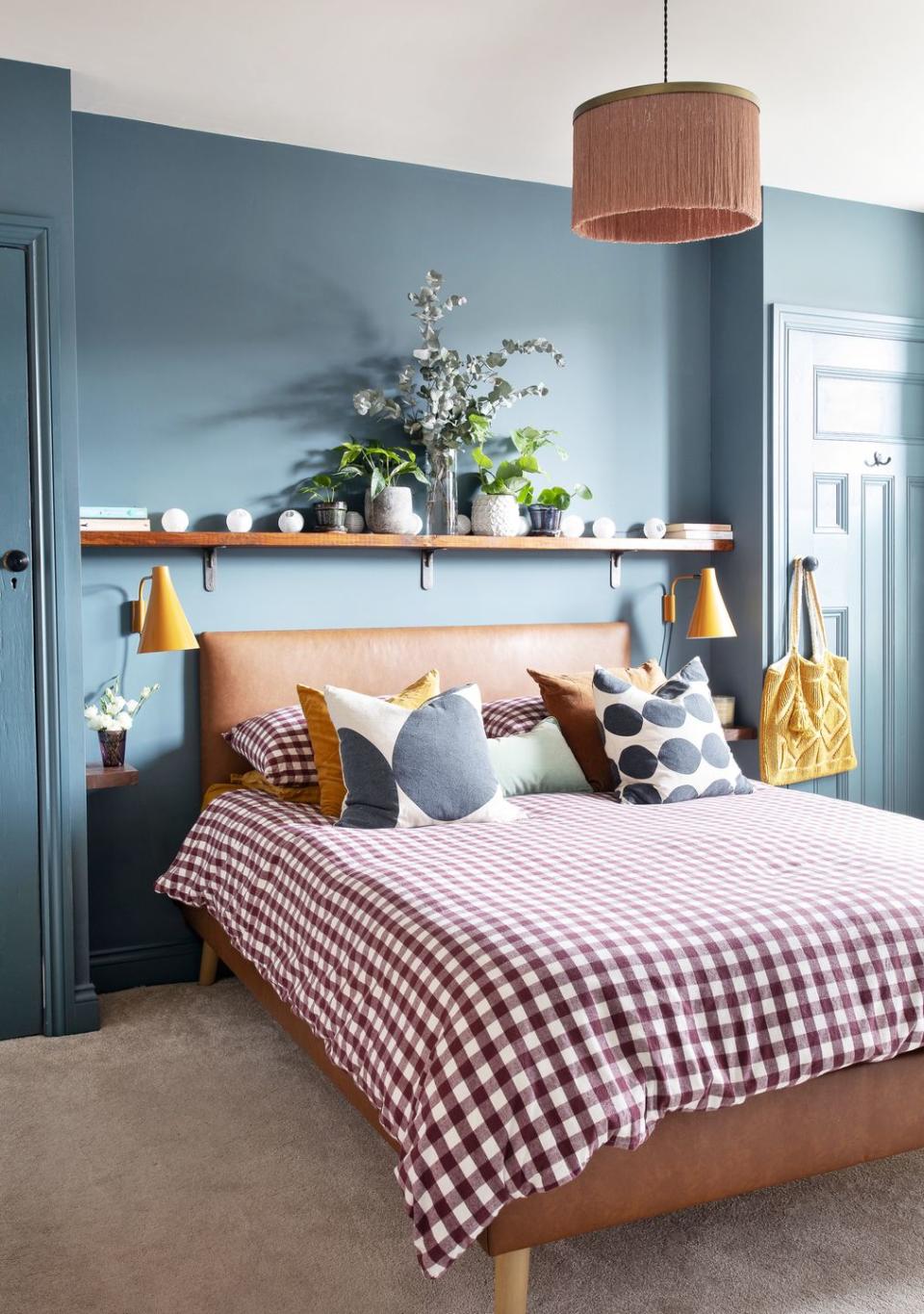 bedroom painted in deep teal blue with leather upholstered bed with gingham bedlinen