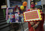 A teacher wearing face mask as a precaution against the coronavirus holds a placard that reads 'let's chase away coronavirus pandemic and get back students to school for education' outside Blossoms High School in Bengaluru, India, Friday, Jan. 1, 2021. The southern state of Karnataka on Friday opened schools for students of grade 10 and 12 after a gap of more than nine months. India has more than 10 million cases of coronavirus, second behind the United States. (AP Photo/Aijaz Rahi)