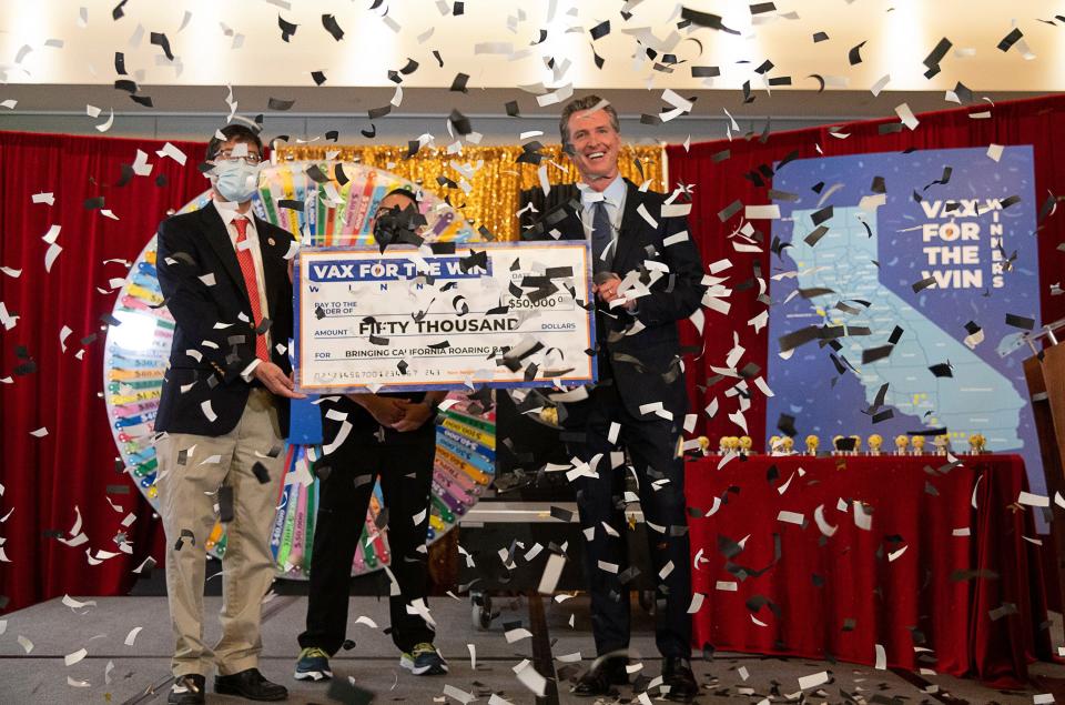 Gov. Gavin Newsom, State Sen. Richard Pan, left, and UC Davis Assistant Nurse Manager Claudio Alvarado, center, hold a mock check as the state drew the first 15 winners to be awarded $50,000 for getting vaccinated against COVID-19 on Friday in Sacramento.