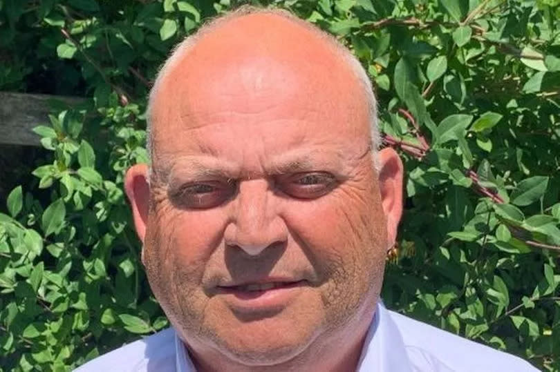 Man in light blue shirt in front of hedge