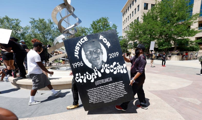 In this June 27, 2020, file photo, demonstrators carry a giant placard outside the police department in Aurora, Colo. during a rally and march over the death of Elijah McClain. (AP Photo/David Zalubowski, File)