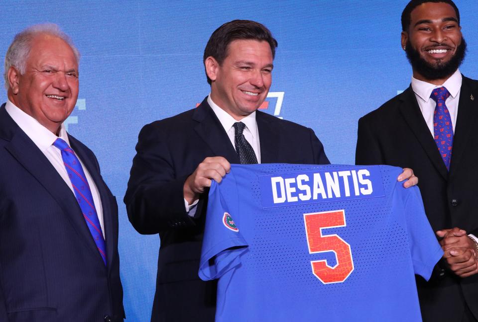 UF Board of Trustees Chair Mori Hosseini stands beside Gov. Ron DeSantis as he holds up a jersey he received during a ceremony at Alumni Hall on the UF campus on Sept. 13, 2021.