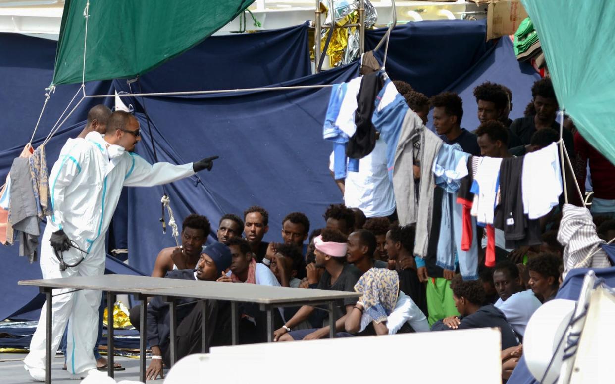 <span class="caption">An Italian official gestures at migrants waiting to disembark in the Sicilian port of Catania in August 2018.</span> <span class="attribution"><a class="link " href="https://www.gettyimages.com/detail/news-photo/an-official-wearing-a-protective-suit-gestures-towards-news-photo/1021751110" rel="nofollow noopener" target="_blank" data-ylk="slk:Giovanni Isolino/AFP via Getty Images;elm:context_link;itc:0;sec:content-canvas">Giovanni Isolino/AFP via Getty Images</a></span>