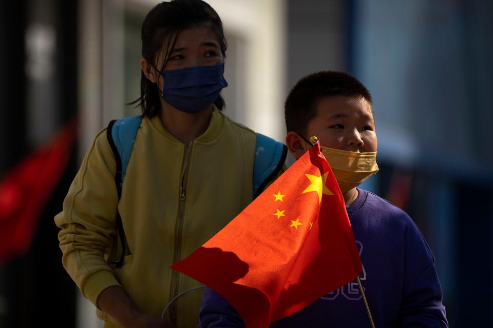 A boy wearing a face mask carries a Chinese flag as he walks along a pedestrian shopping street in Beijing on Oct. 6, 2022. China has announced its first overall population decline in recent years amid an aging society and plunging birthrate.