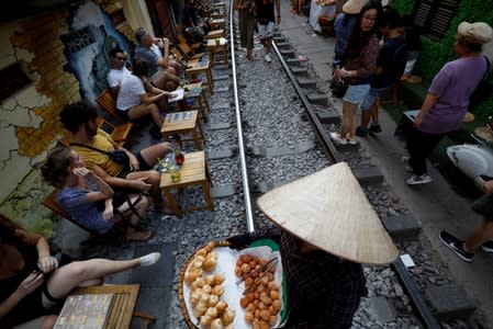 A woman sells snacks as tourists sit at tables for drinks along the railway at the Old Quarter in Hanoi, Vietnam