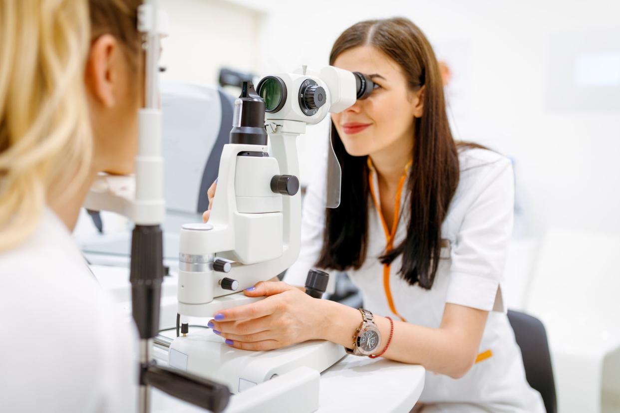 Female ophtalmologist looking throught eye test equipment and checking female patient's eyesight