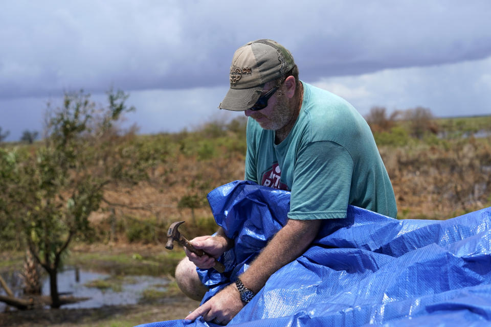 Mark Poindexter puts a tarp on the damaged roof of his home in in Gulf Breeze, La., in the aftermath of Hurricane Laura, Saturday, Aug. 29, 2020. (AP Photo/Gerald Herbert)