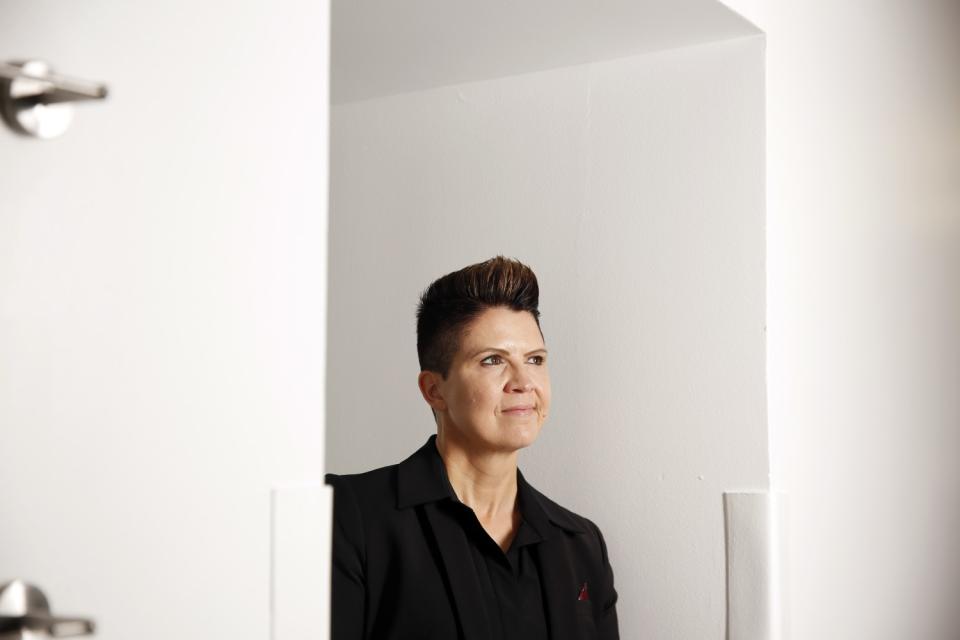 A woman wearing a dark top and jacket stands in an alcove between two white walls.