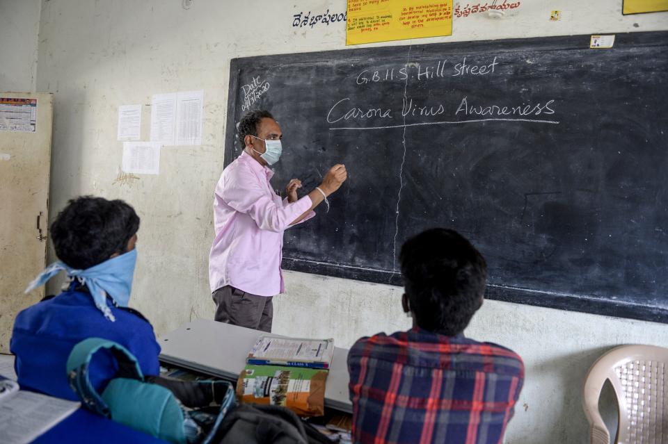 A teacher (C) wearing a facemask teaches as students attend the class at a governement-run high school in Secunderabad.
