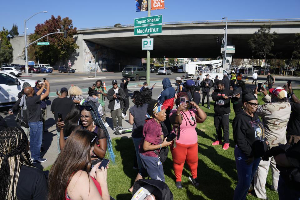 People take pictures and gather beneath a new sign during a street renaming ceremony for Tupac Shakur in Oakland, Calif., Friday, Nov. 3, 2023. A stretch of street in Oakland was renamed for Shakur, 27 years after the killing of the hip-hop luminary. A section of Macarthur Boulevard near where he lived in the 1990s is now Tupac Shakur Way, after a ceremony that included his family members and Oakland native MC Hammer. (AP Photo/Eric Risberg)