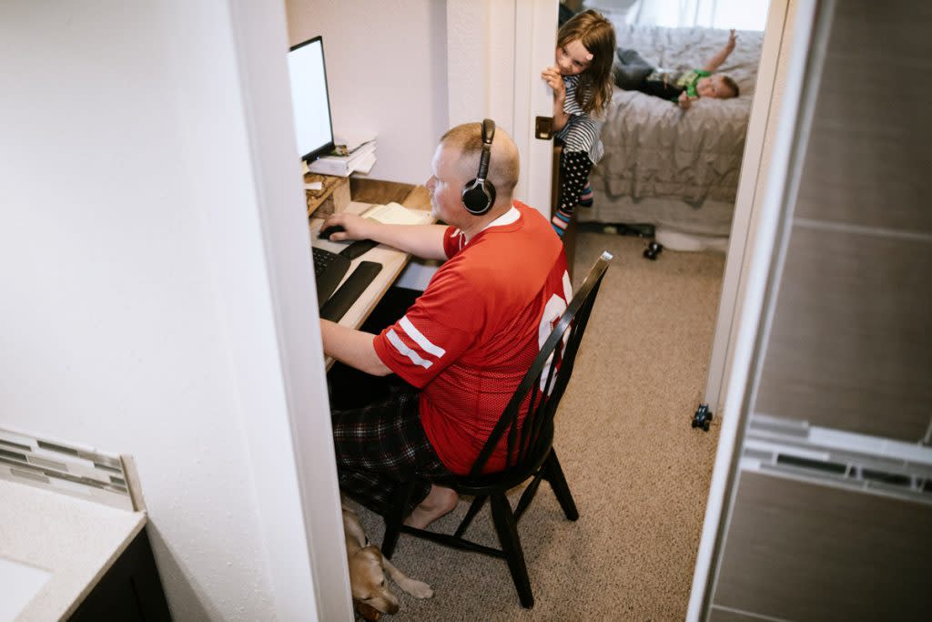 A completes his work from an office set up in his closet at home as his kids spend time in his room beside him. This photo illustrates one way to maximize small spaces: put your office in your closet.