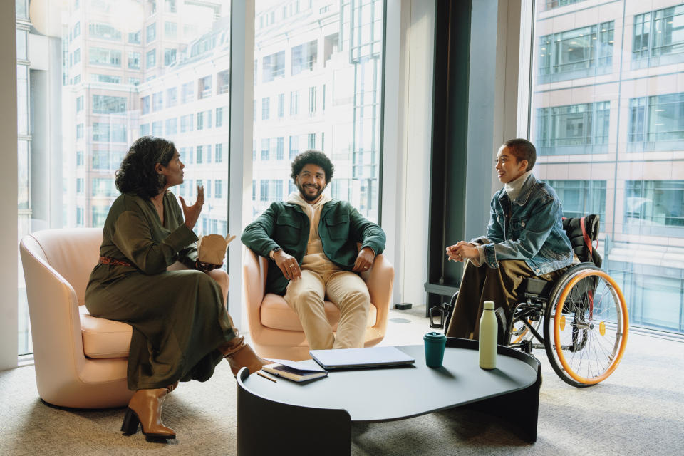 Three people talking together in an office; two sit in chairs, one sits in a wheelchair