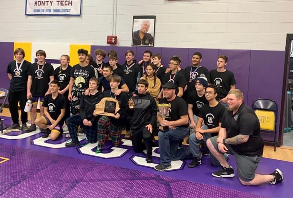 The Monty Tech wrestling team gathers together for a team photo underneath a picture of late Bulldogs head coach Kieron Smith after winning the tournament it held in his memory, Saturday, inside Bulldog Gym in Fitchburg.