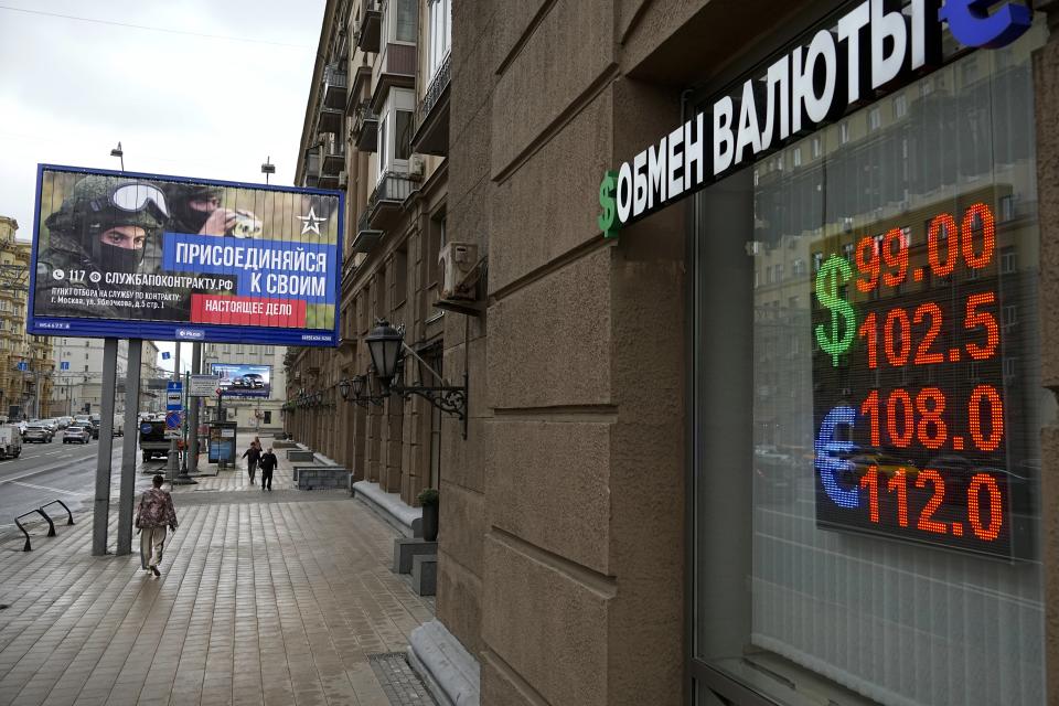 People walk past a currency exchange office with an army recruiting billboard calling for a contract for service in the Russian armed forces in Moscow, Russia, Monday, Aug. 14, 2023. The Russian ruble has reached its lowest value since the early weeks of the war in Ukraine as Western sanctions weigh on energy exports and weaken demand for the national currency. The Russian currency passed 101 rubles to the dollar on Monday, continuing a more than 25% decline in its value since the beginning of the year. (AP Photo/Alexander Zemlianichenko)