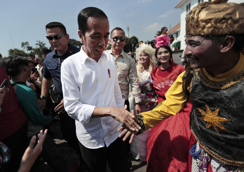 Indonesian President Joko Widodo, center, is greeted by a street busker during his visit at the Old Town in Jakarta, Indonesia, Friday, July 26, 2019. Indonesian President Joko Widodo said in an interview Friday that he will push ahead with sweeping and potentially unpopular economic reforms, including a more business-friendly labor law, in his final term because he is no longer constrained by politics. (AP Photo/Dita Alangkara)